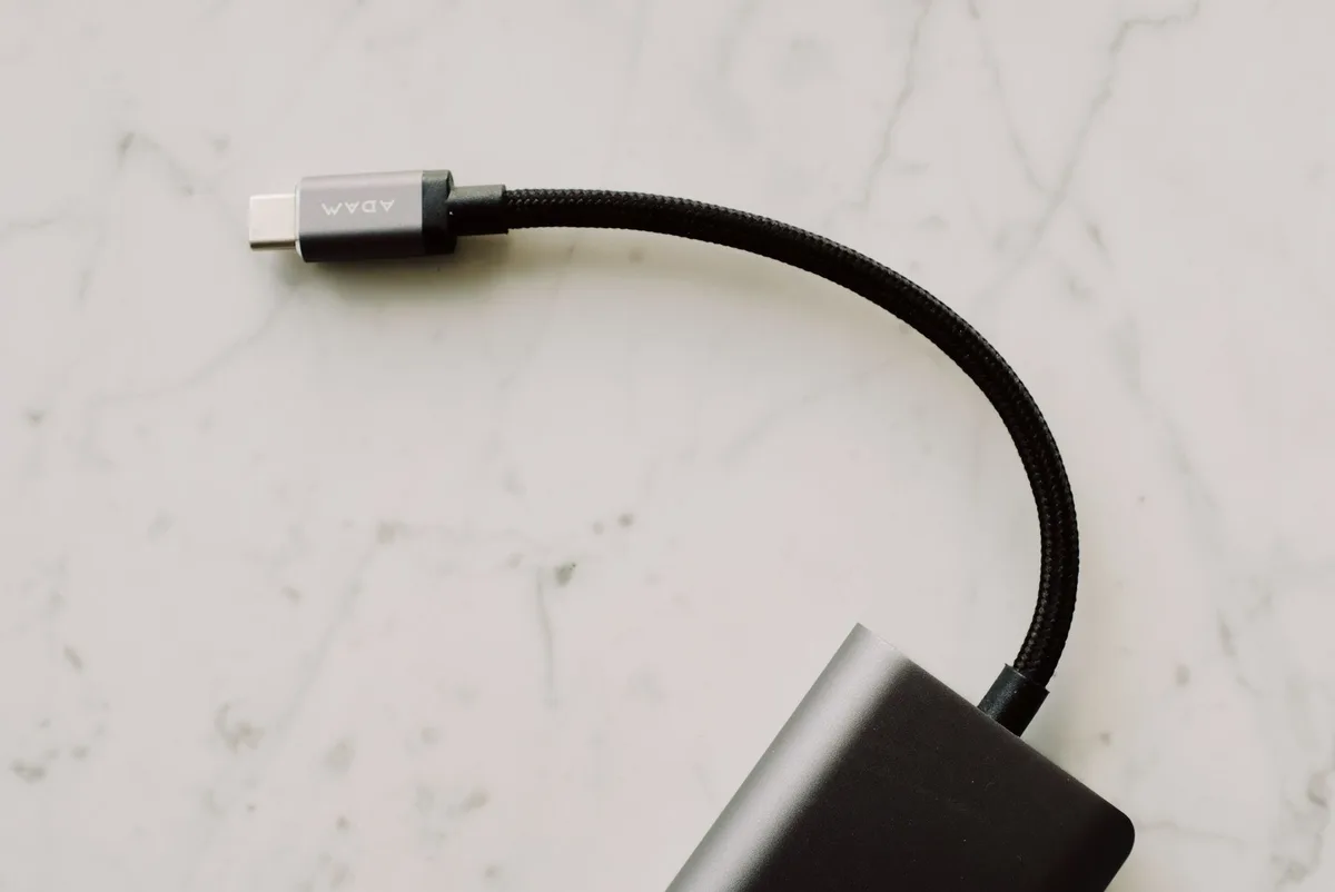 Smartphone mit USB-Adapter verbunden, neben Tastatur und Maus auf Schreibtisch