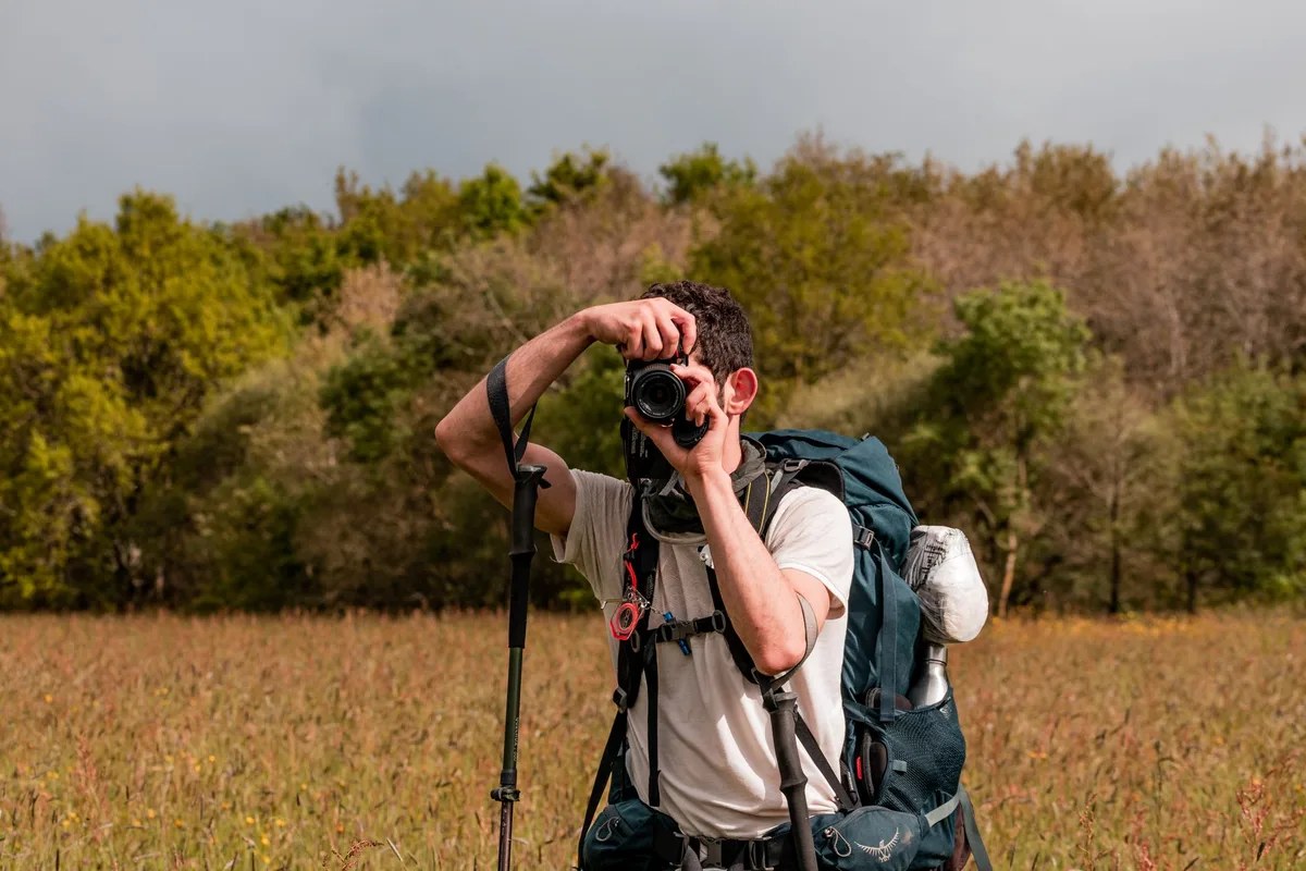 Wanderer mit Fotorucksack und kompaktem Stativ in Naturlandschaft
