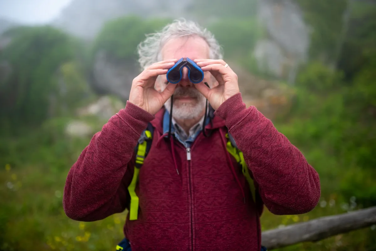 Wanderer beobachtet mit Fernglas die Natur in einer offenen Landschaft