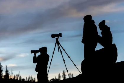Outdoor-Fotograf mit Kamera und Stativ am Bergsee bei Dämmerung
