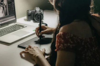 Person bearbeitet ein Foto mit Rauschreduktionssoftware auf dem Laptop während eine Kamera auf dem Schreibtisch liegt