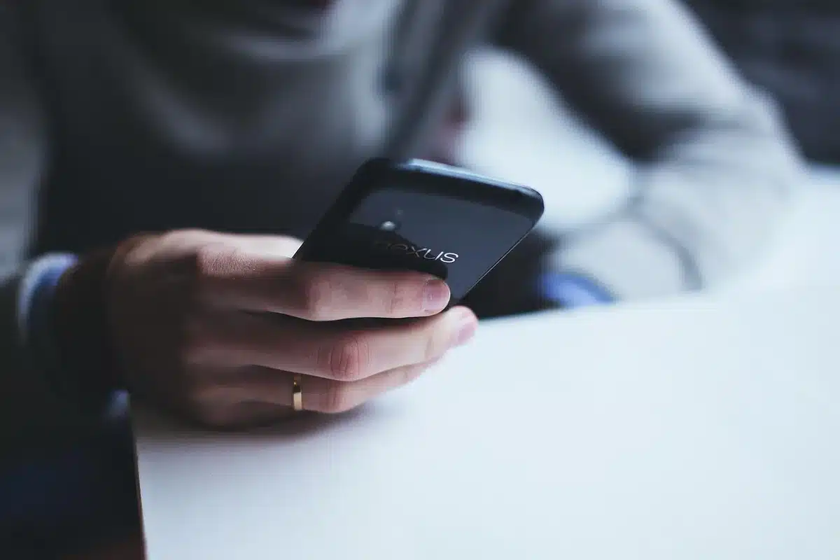 Hände halten ein Smartphone über einen WLAN-Drucker, während ein gedrucktes Dokument aus dem Ausgabefach kommt.