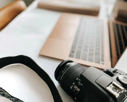 Kameraobjektiv neben Laptop und USB‑C‑Kabel auf einem Schreibtisch, Tageslicht