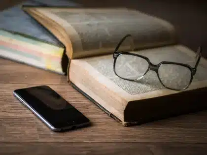 Anonymes Smartphone liegt auf Tisch, Hände zeigen auf technische Spezifikationen in einer Broschüre