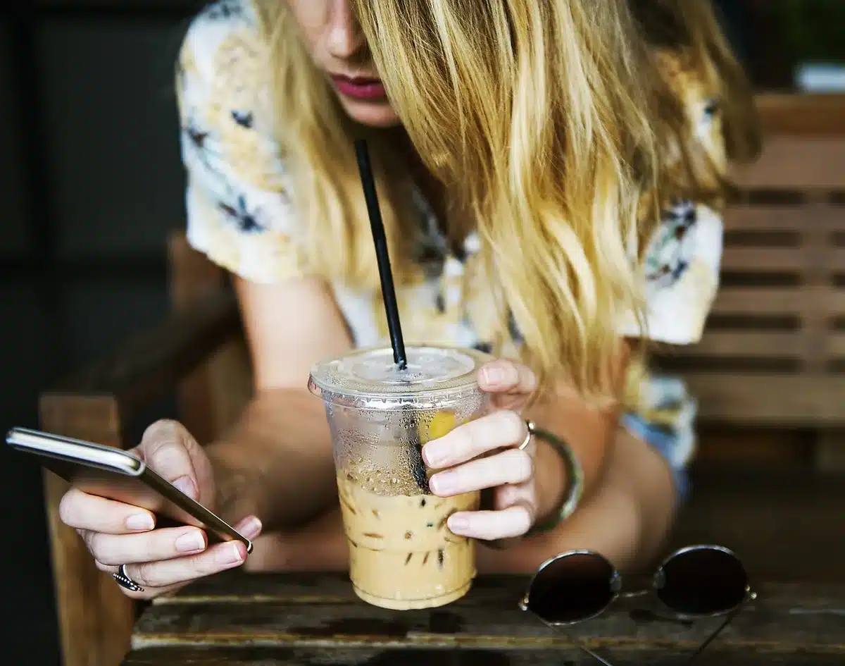 Smartphone mit WhatsApp-ähnlicher Nachrichtenliste auf einem Café-Tisch, unscharfe Hände im Hintergrund